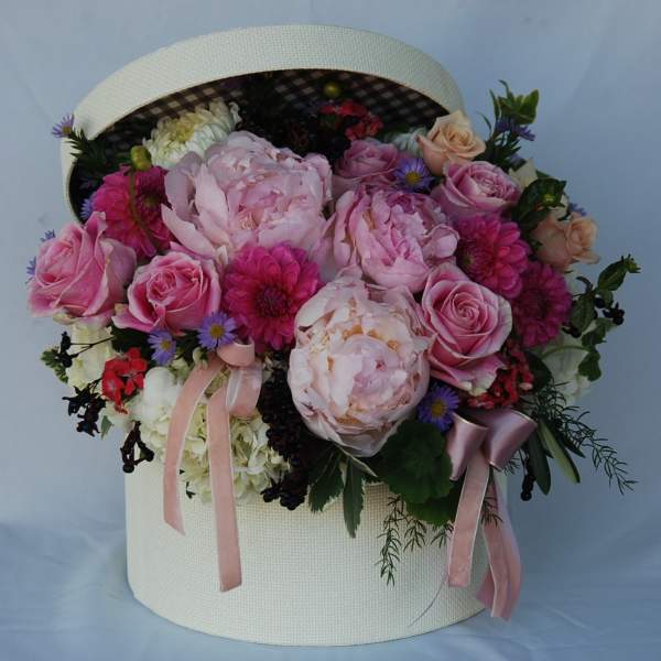 Pink and white floral arrangement in a round hatbox with ribbons