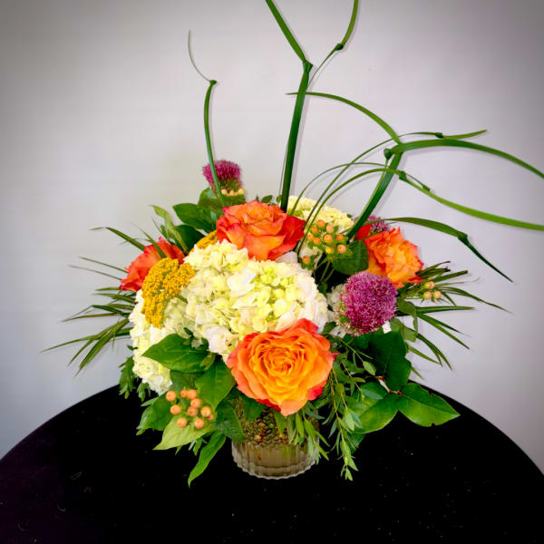 Orange roses and white hydrangeas in a glass vase with tall grass accents
