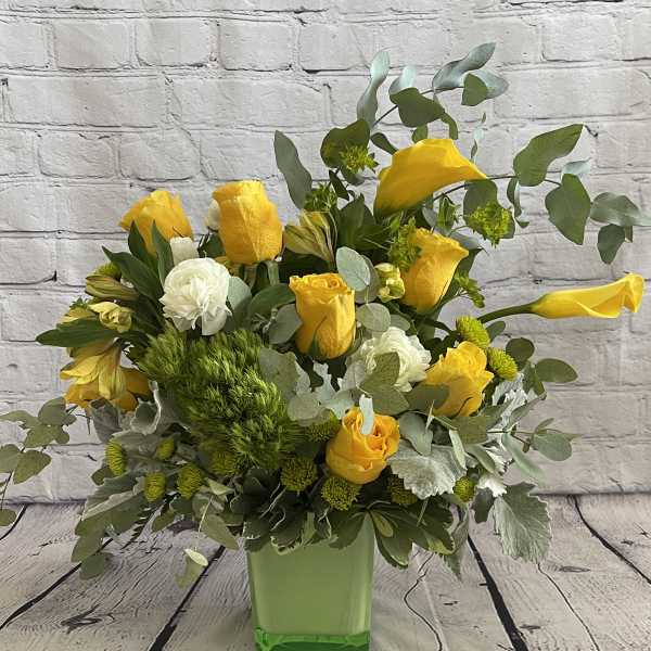 Yellow roses and white blooms arranged in a green square vase