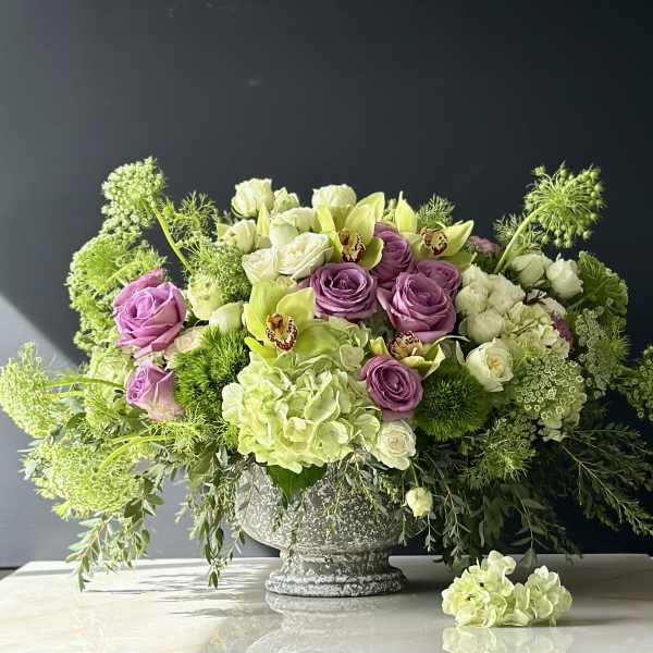 Lavender roses and pale green flowers in a gray pedestal vase