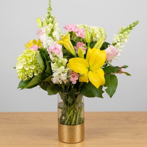 Bouquet of yellow lilies, pink roses, and white blooms in a glass vase