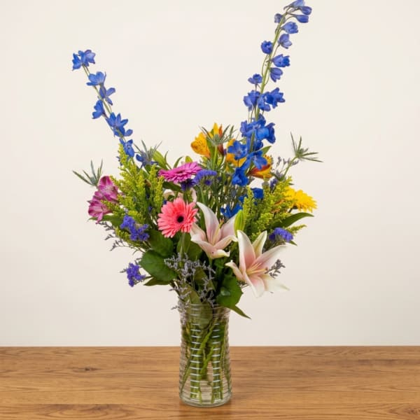 Mixed bouquet of blue, pink, yellow, and white flowers in a glass vase
