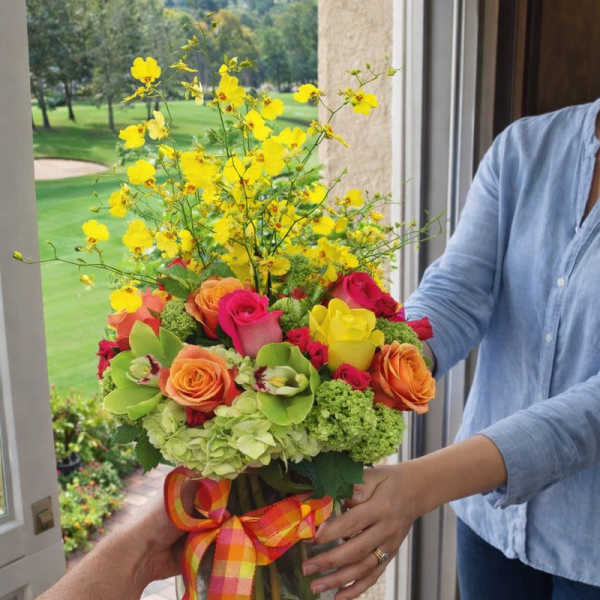 Colorful bouquet of roses and yellow orchids in a glass vase with ribbon