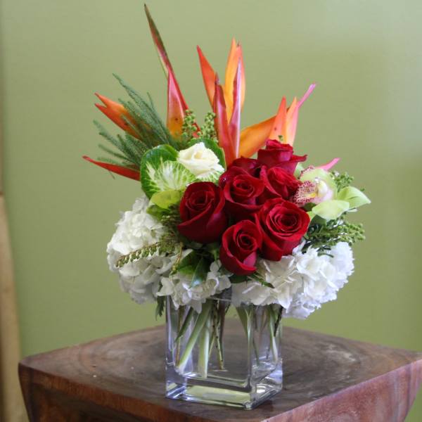 Red roses and white hydrangeas in a clear glass vase with orange tropical blooms