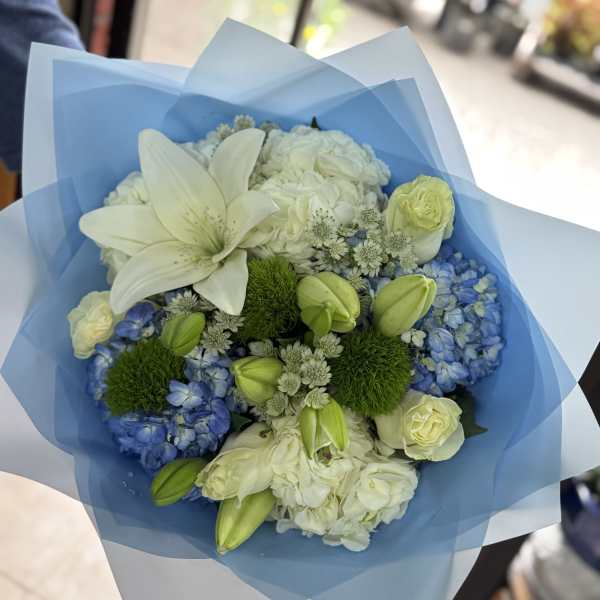 Bouquet of white lilies, blue hydrangeas, and pale roses wrapped in blue paper
