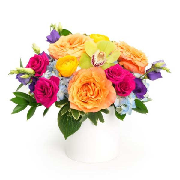 Low round arrangement of orange roses and bright mixed blooms in a white cylinder vase