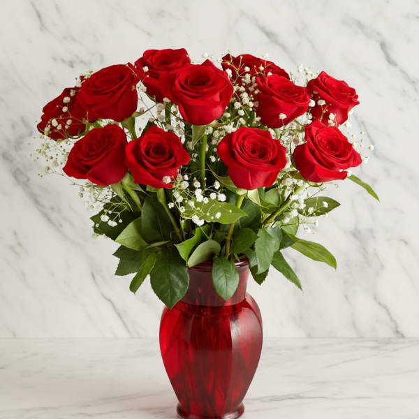 Red roses arranged in a red glass vase with baby's breath