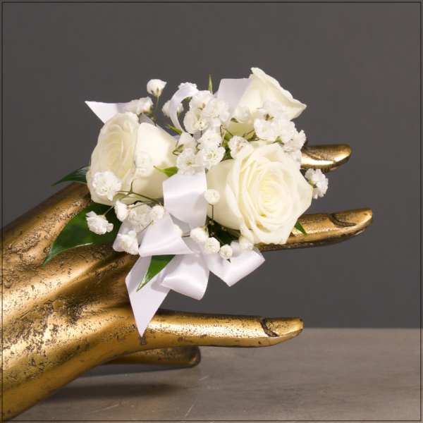 White rose corsage with baby's breath and ribbon on a gold hand display