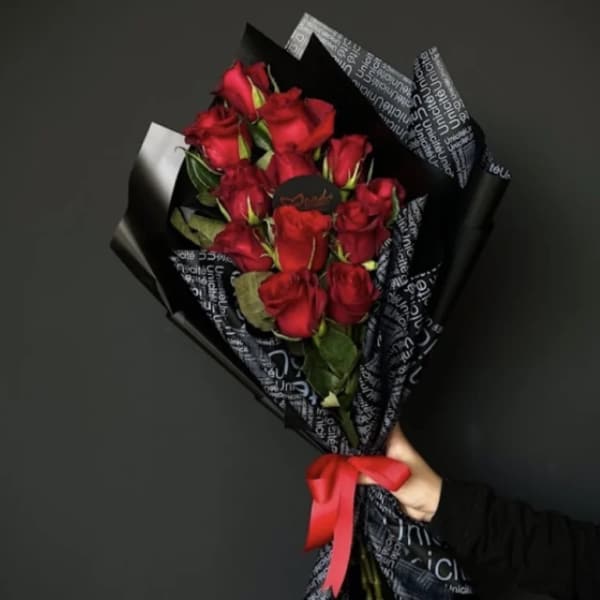 Handheld bouquet of red roses wrapped in black paper with a red ribbon