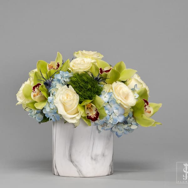 White roses and blue hydrangeas in a white vase with green orchids