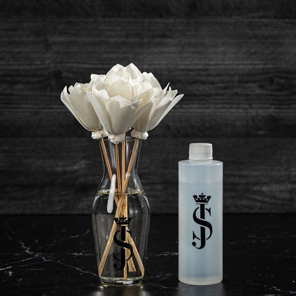 White artificial flowers in a clear glass vase beside a frosted bottle