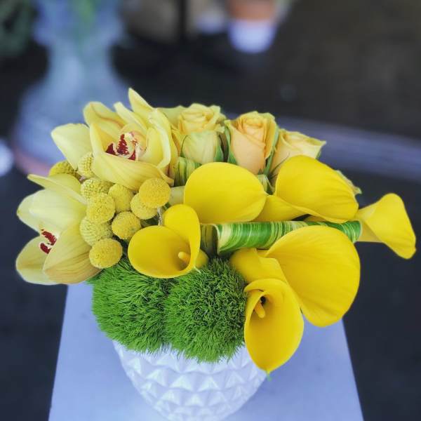 Yellow calla lilies and roses in a white textured vase
