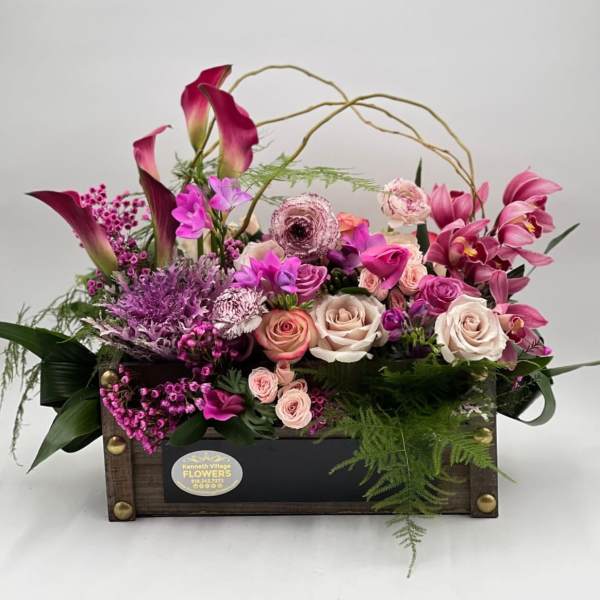 Pink and purple floral arrangement in a wooden box with roses and calla lilies
