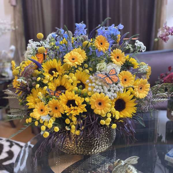 Mixed bouquet of yellow sunflowers and gerbera daisies in a gold vase