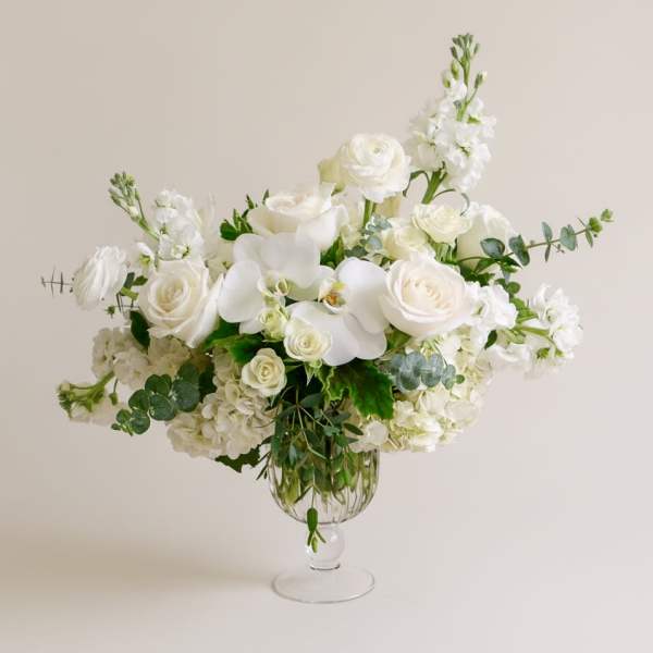White floral arrangement in a clear glass vase with roses and orchids