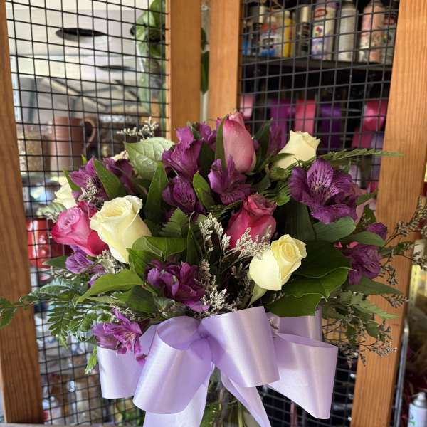 Bouquet of pink, white, and purple flowers in a glass vase with a lavender ribbon