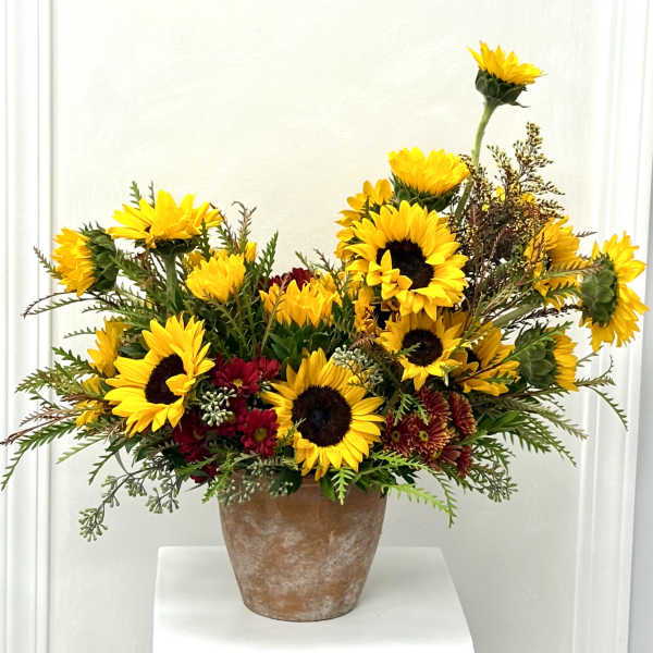 Arrangement of yellow sunflowers and red chrysanthemums in a rustic clay pot
