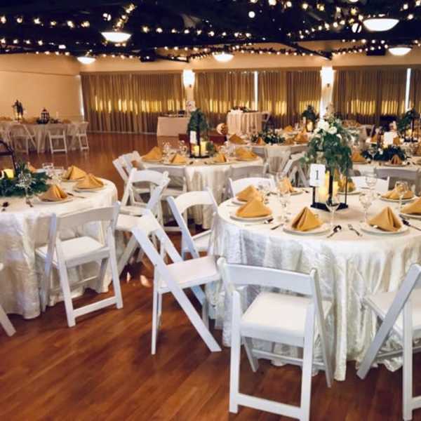Round banquet tables with white chairs and small floral centerpieces in a reception hall