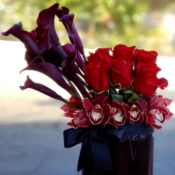 Red roses and purple calla lilies in a tall glass vase