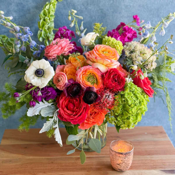 Colorful mixed flower arrangement in a glass vase with a candle beside it