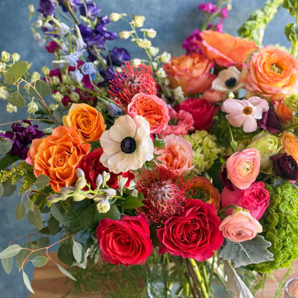 Colorful mixed bouquet of roses, ranunculus, and other blooms in a glass vase