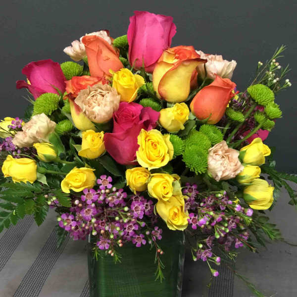 Mixed roses in a square glass vase with purple filler flowers