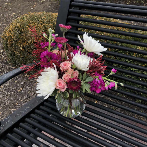 Pink and white flowers arranged in a clear glass vase on a black bench.