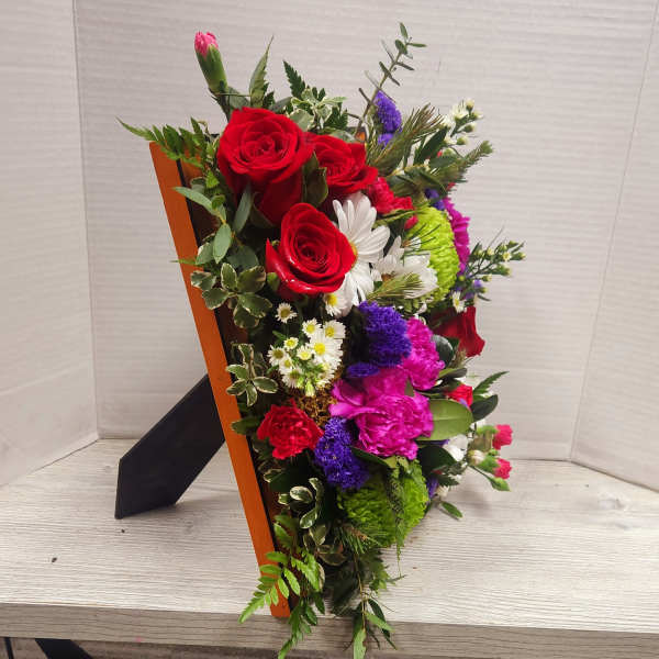 Mixed bouquet with red roses, pink carnations, and white daisies in a wooden holder