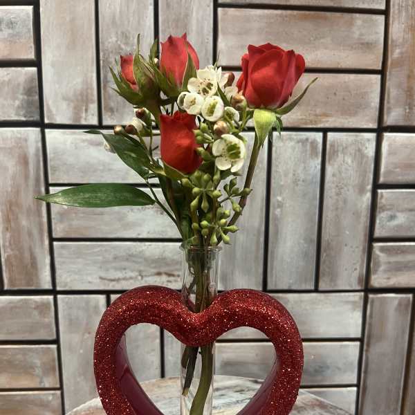 Red roses and white filler flowers in a glass tube vase with a glittery heart base