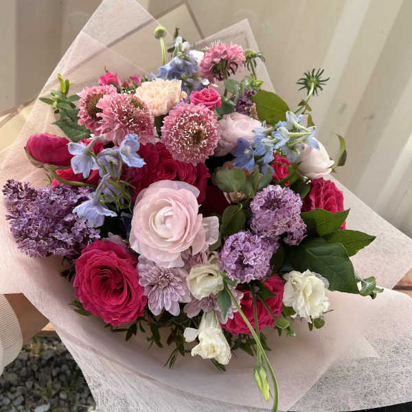Hand-tied bouquet of pink, purple, and white flowers wrapped in pale paper