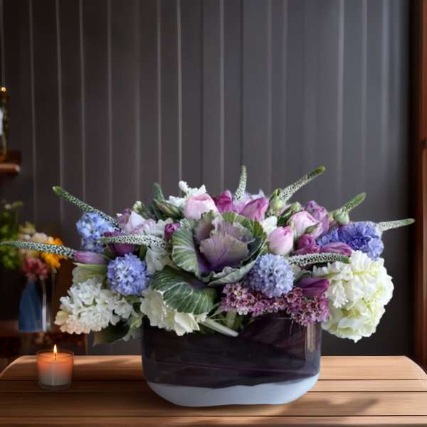 Lavender and white floral arrangement in a low rectangular vase beside a candle