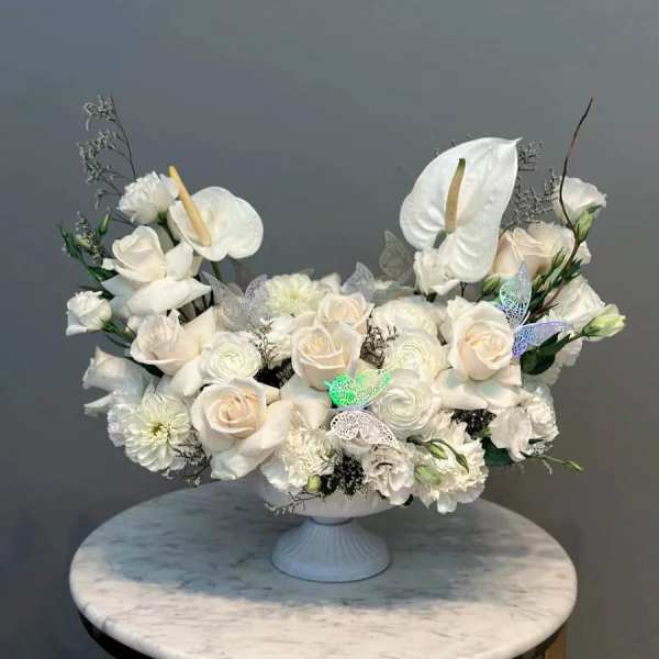 White floral arrangement in a pedestal vase with roses and anthuriums