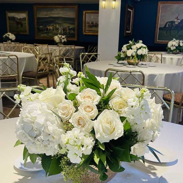 White rose and hydrangea centerpiece in a low bowl on a round table