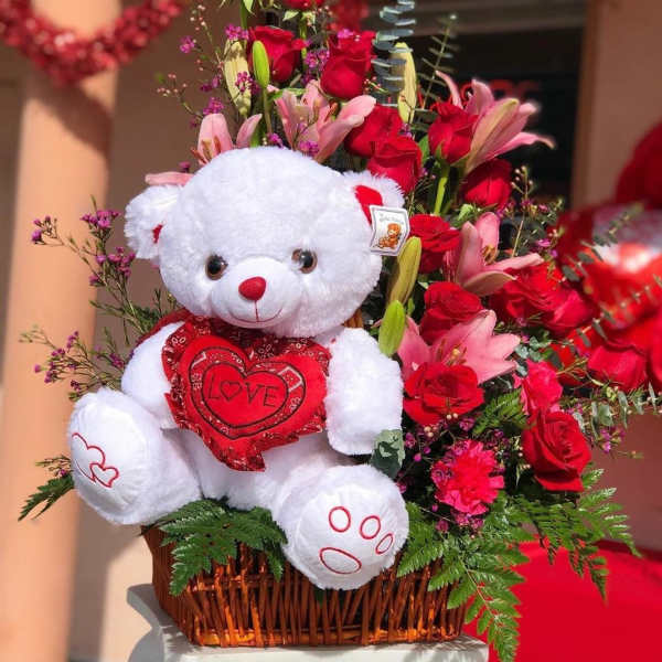 Red roses, pink lilies, and medium plush bear in basket.