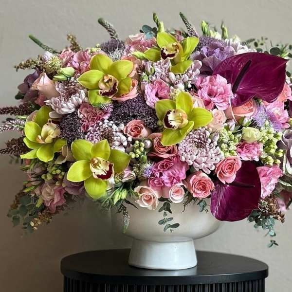 Large mixed bouquet in a white pedestal vase with pink, purple, and lime flowers