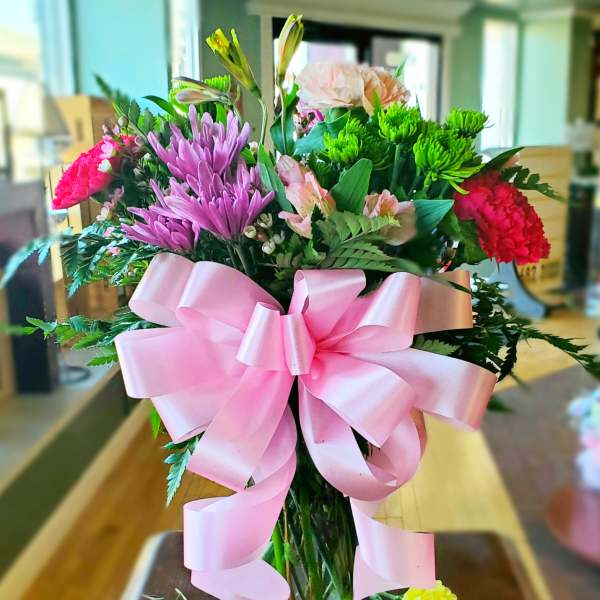 Mixed bouquet in a glass vase with a large pink ribbon