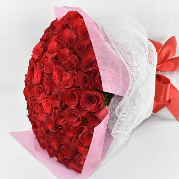 Large bouquet of red roses wrapped in pink paper and white mesh with a red satin bow