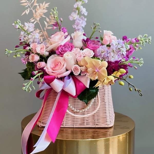 Pink and lavender floral arrangement in a woven basket with ribbon