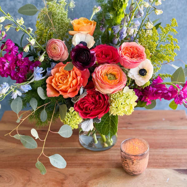 Mixed bouquet of roses and other blooms in a glass vase with a candle nearby