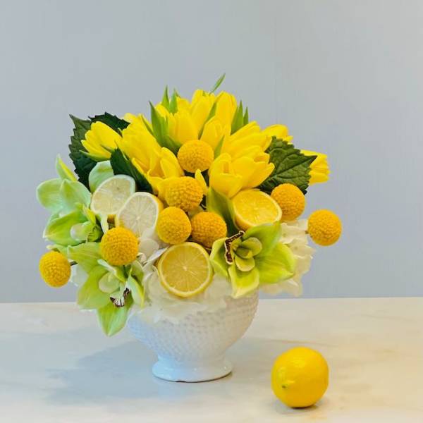 Yellow flowers and citrus slices arranged in a white vase