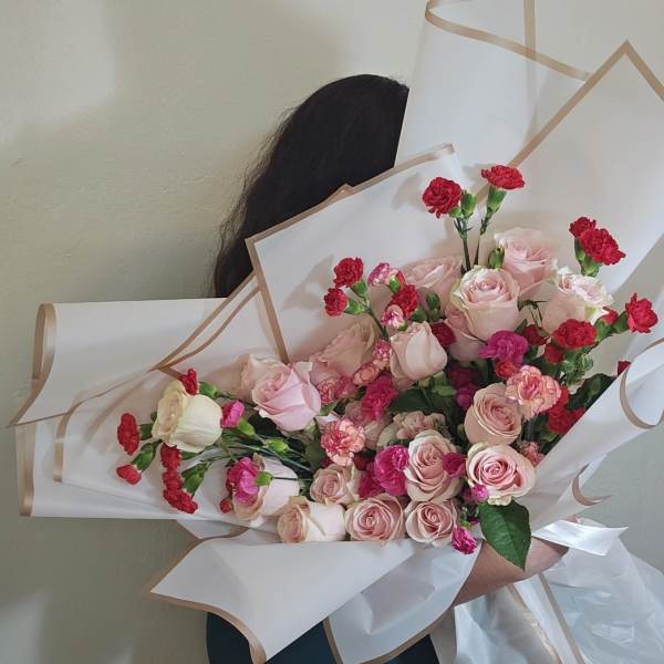 Bouquet of pink roses and red carnations wrapped in white paper