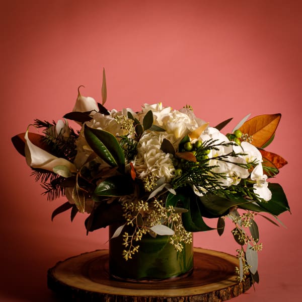 White floral arrangement in a dark green vase with broad leaves