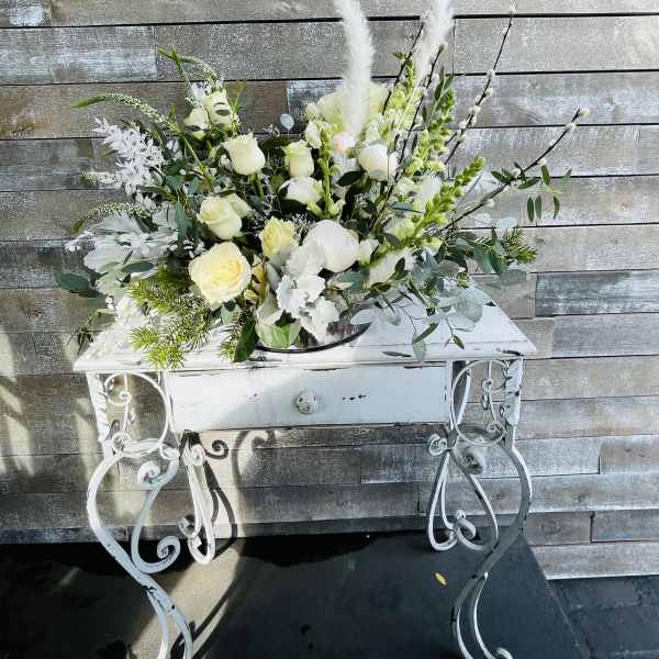 White rose arrangement with tall feather accents in a white metal stand