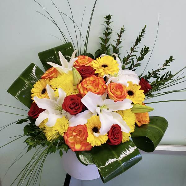 Bouquet of red and orange roses with white lilies and yellow daisies in a white vase