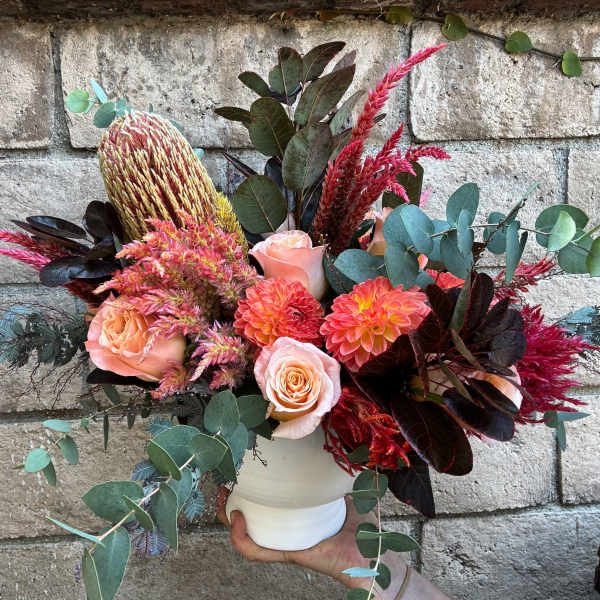 Bouquet of peach roses, coral dahlias, and pink-red blooms in a white vase