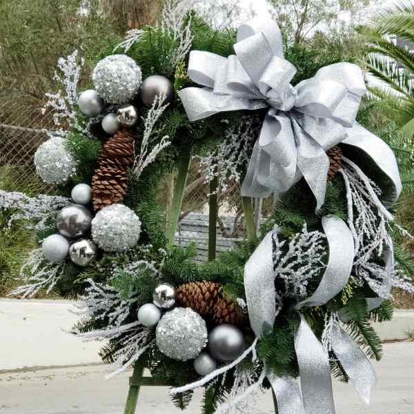 Holiday wreath with silver ornaments, pinecones, and a large silver bow