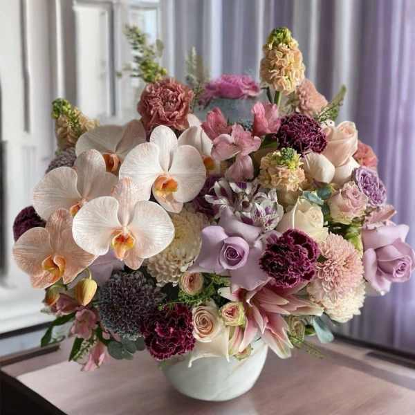 Pastel bouquet with orchids, roses, and carnations in a white vase