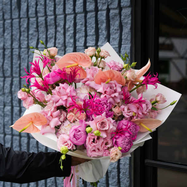 Pink and peach bouquet with anthuriums, roses, and lisianthus wrapped in white paper
