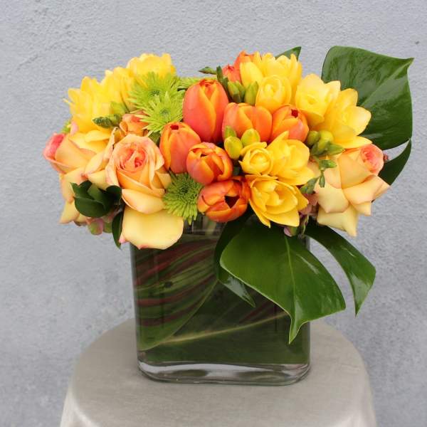 Yellow and orange tulips with roses in a square glass vase
