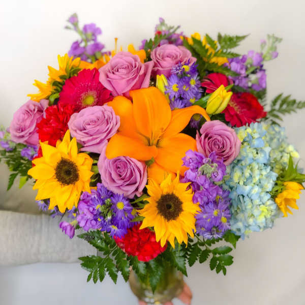 Colorful bouquet with roses, lilies, sunflowers, and hydrangeas in a glass vase
